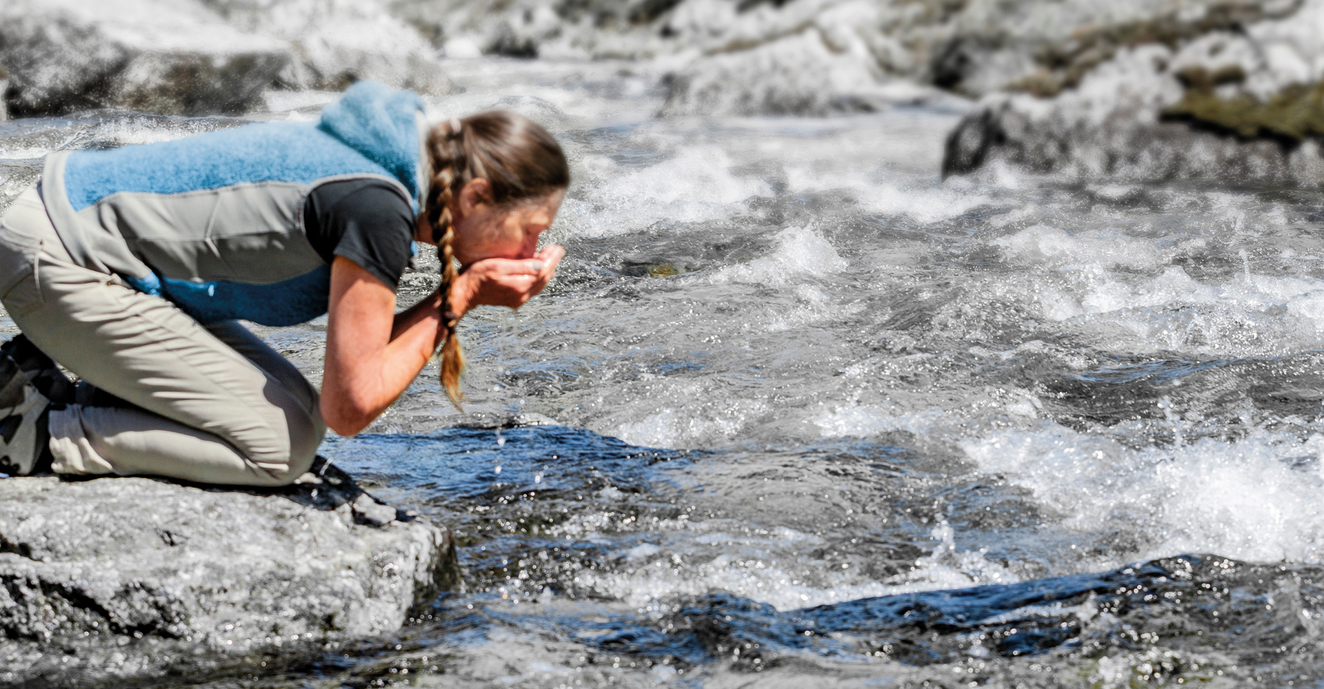 Eine Frau trinkt Wasser aus der Bergquelle.